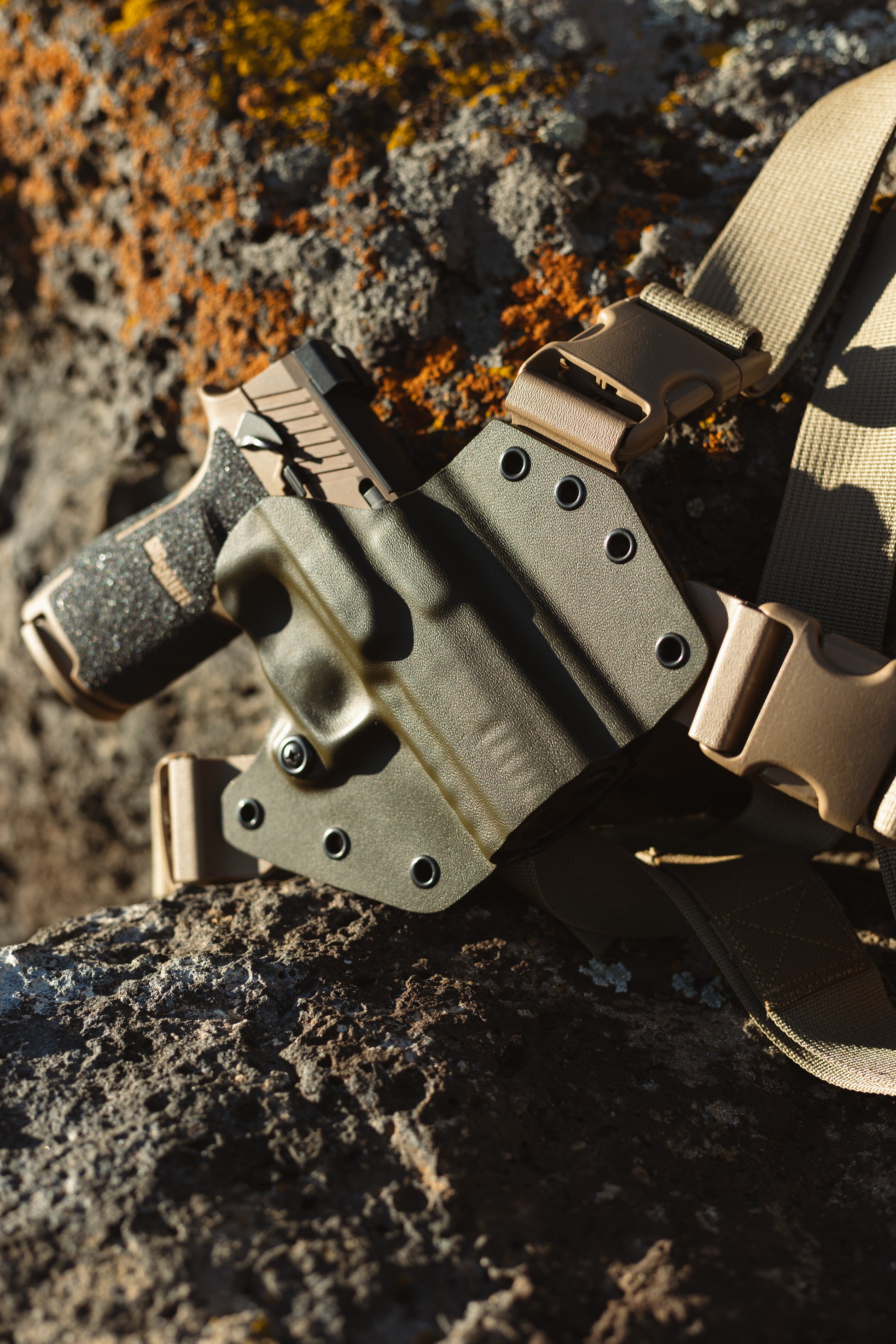 Sig Sauer M18 pistol with thumb safety in an OD green arctos arms chest holster with moss covered rock in background